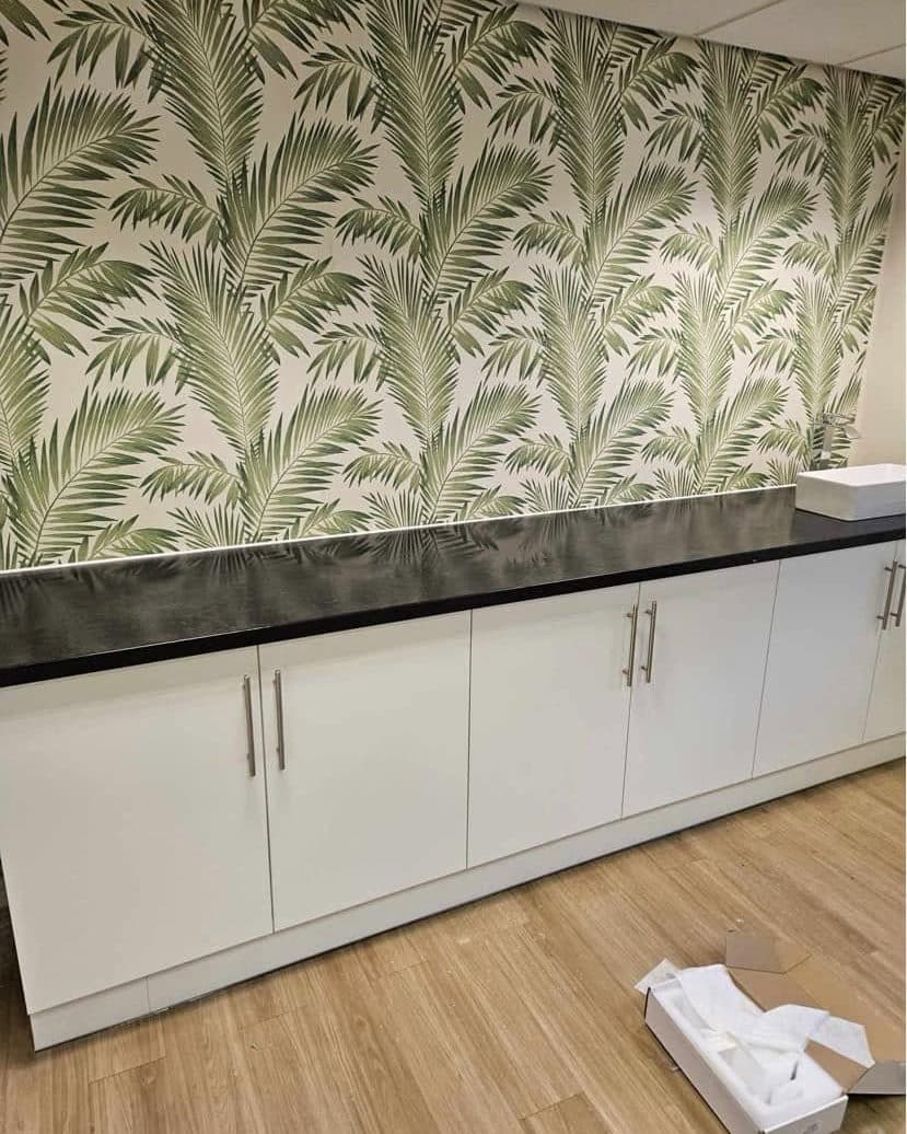 Utility room with white units, black worktop and palm-leaf feature wallpaper