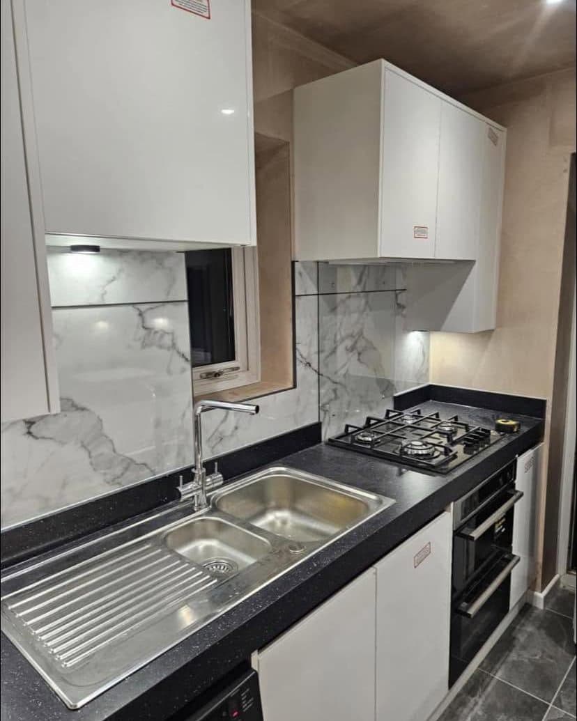 White gloss kitchen with a marble-effect splashback, stainless steel sink and gas hob